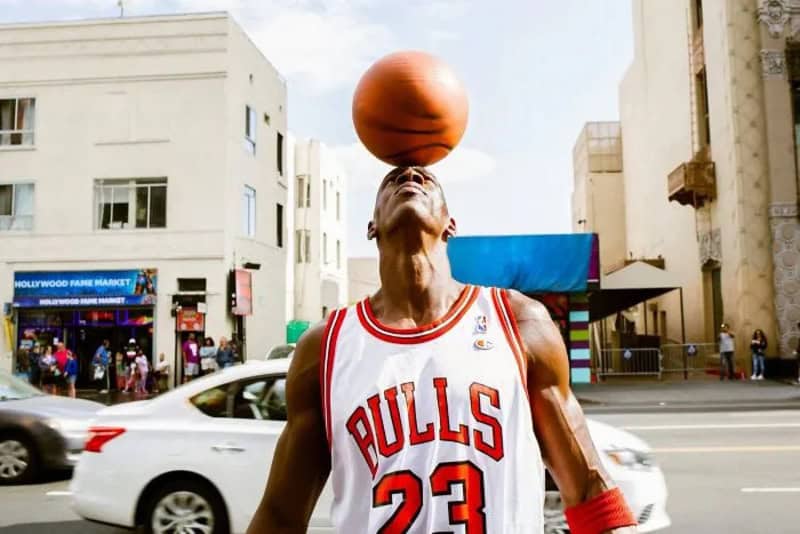 Man in Bulls jersey balancing a basketball on his forehead in downtown LA.