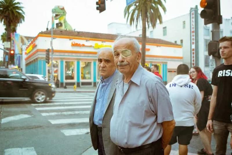 Two elderly men crossing the street in Los Angeles with a colorful building behind them.
