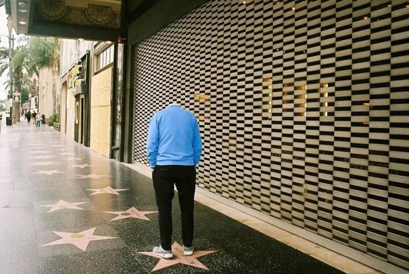 Person in blue hoodie standing on Hollywood Walk of Fame stars.