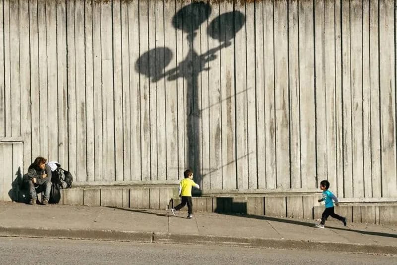 Children running past a wall with a shadow of a streetlamp.