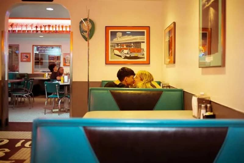 Couple kissing in a retro diner with framed car pictures on the wall.