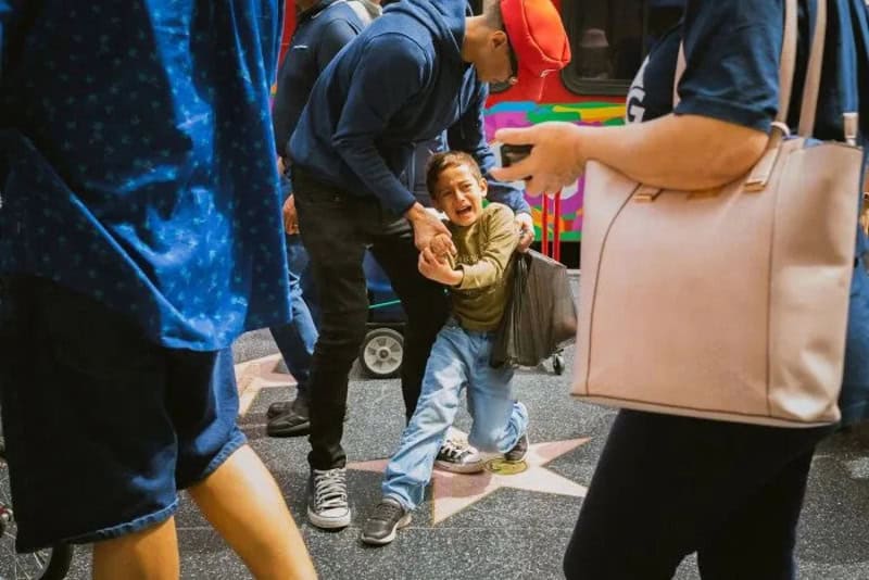 Child crying as adults surround him on a busy street.