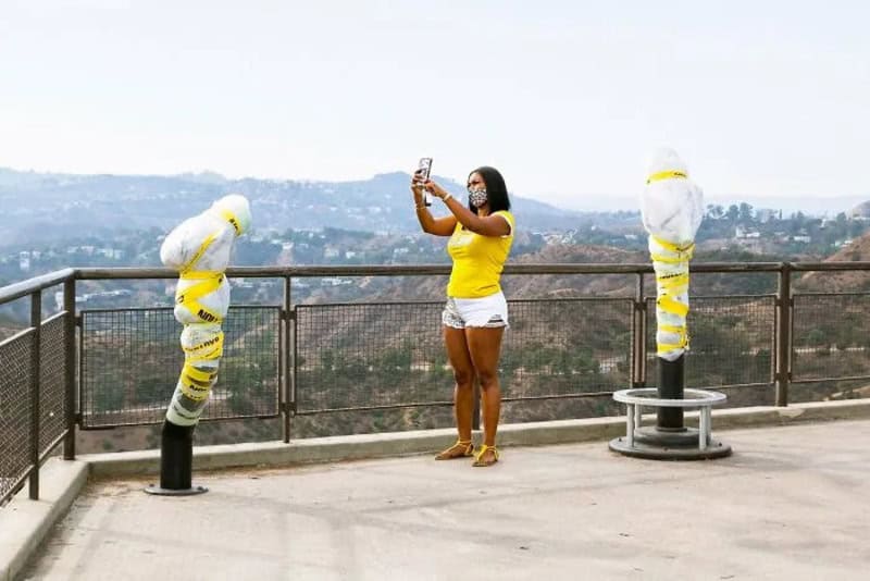 Woman in yellow top and white shorts taking a photo on a viewing platform.