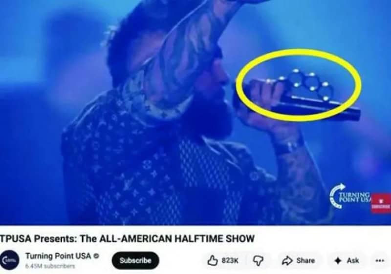 Person holding a microphone with brass knuckles, yellow circle around the knuckles.