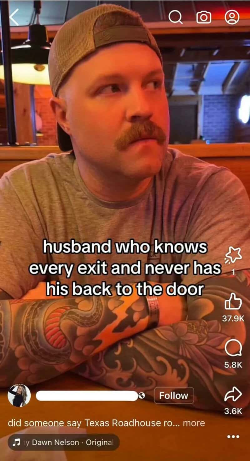 Man with a mustache and tattoos, wearing a cap, sitting in a restaurant.