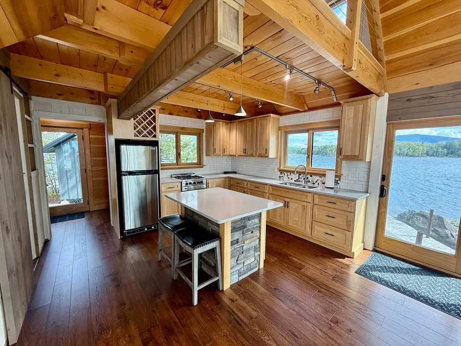 Cozy kitchen with wooden cabinets, island, and lake view through large windows.