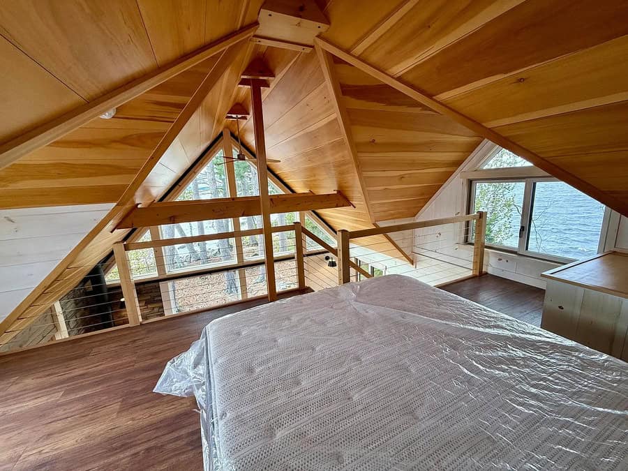 Attic bedroom with wooden walls, sloped ceiling, and large windows.