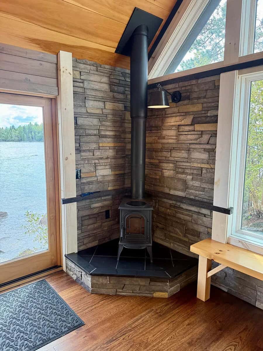 Cozy interior with wood stove and large windows overlooking water.
