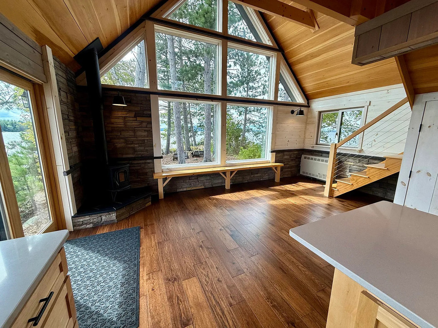 Interior of a modern cabin with large windows, wooden floors, and a staircase.