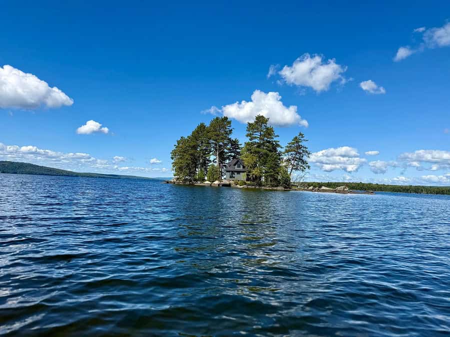 House on an island surrounded by water under a blue sky with clouds.