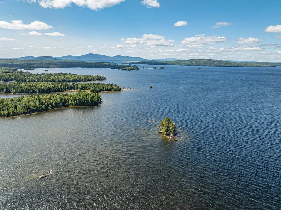 Scenic view of a large lake with small islands and green forests, under a blue sky with clouds.