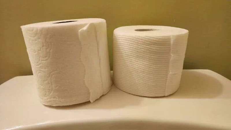 Two rolls of toilet paper on a white surface with a beige background.