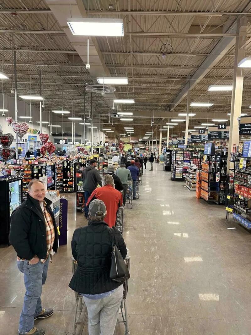 People shopping in a large store with checkout lines and shelves of products.