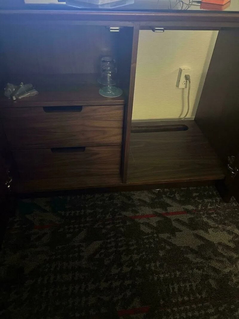 Wooden cabinet with open space and drawers, water bottle on top, plugged into wall socket.