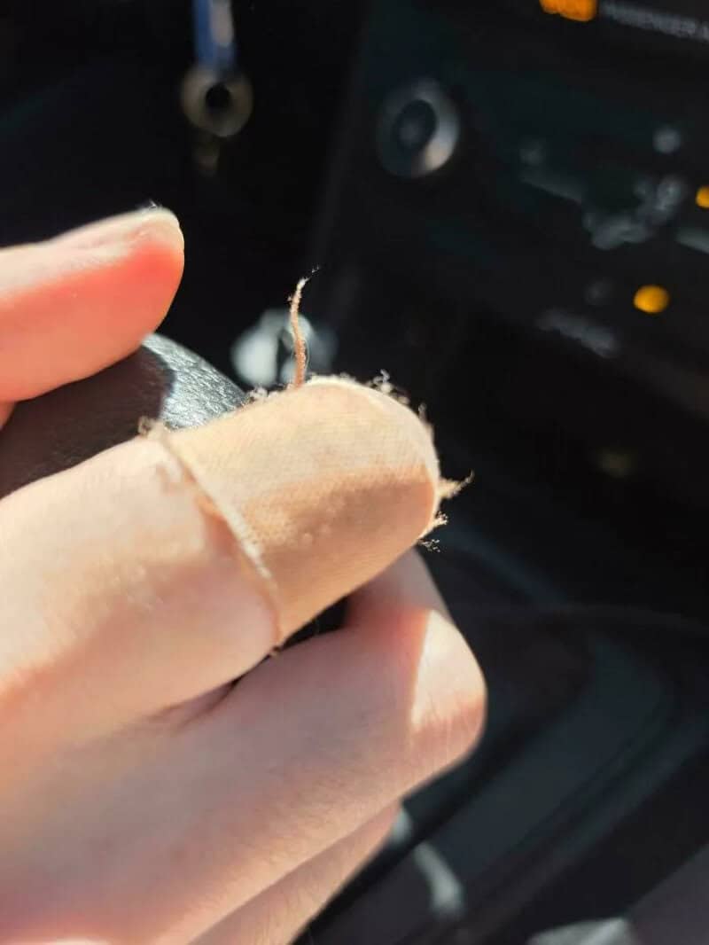 Close-up of a torn finger with a bandage on it inside a car.