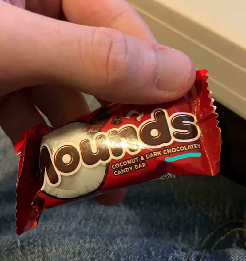 Hand holding a coconut and dark chocolate candy bar in red wrapper.