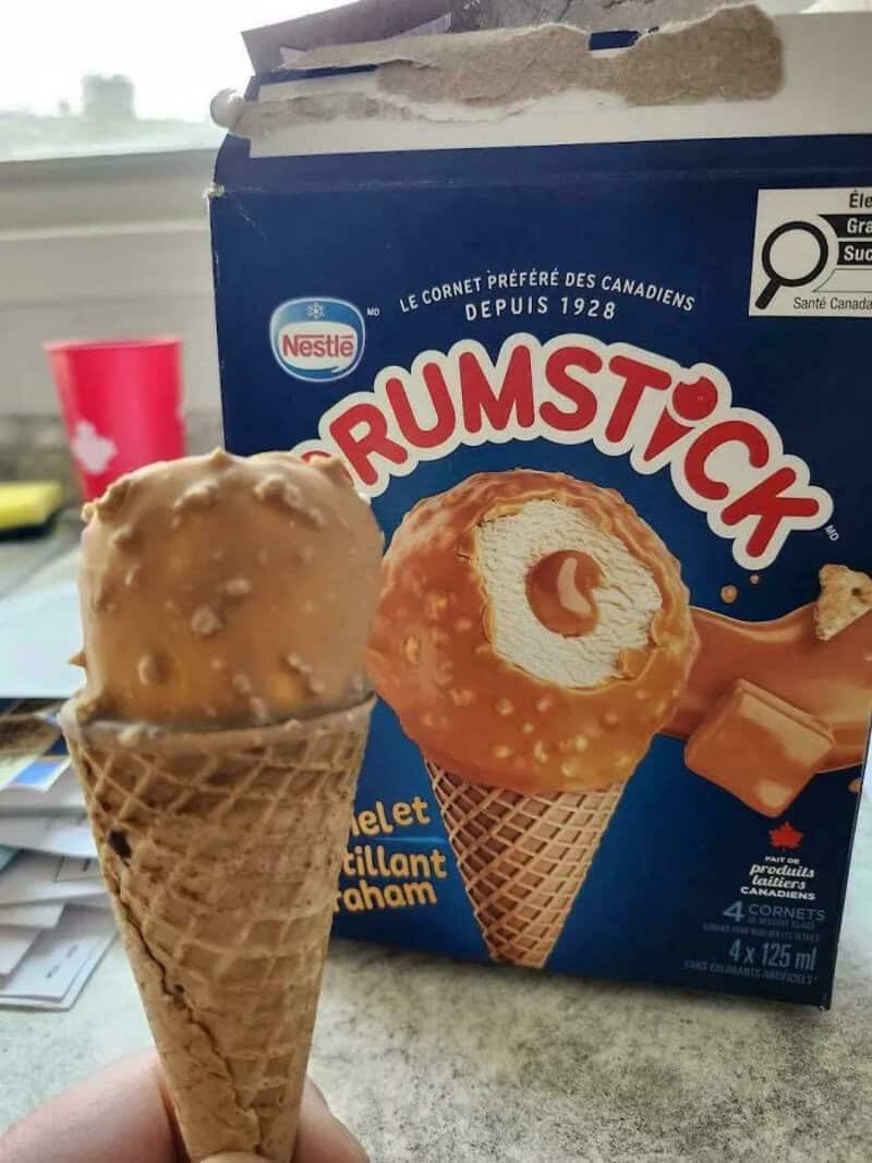 Ice cream cone with caramel flavor next to Rumstick ice cream box on table.
