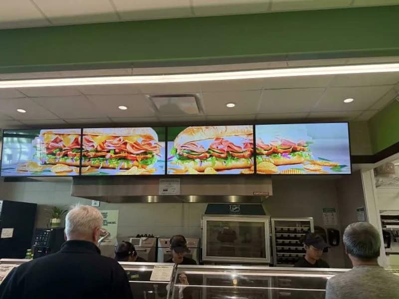 Digital menu screens showing sandwiches in a fast-food restaurant.