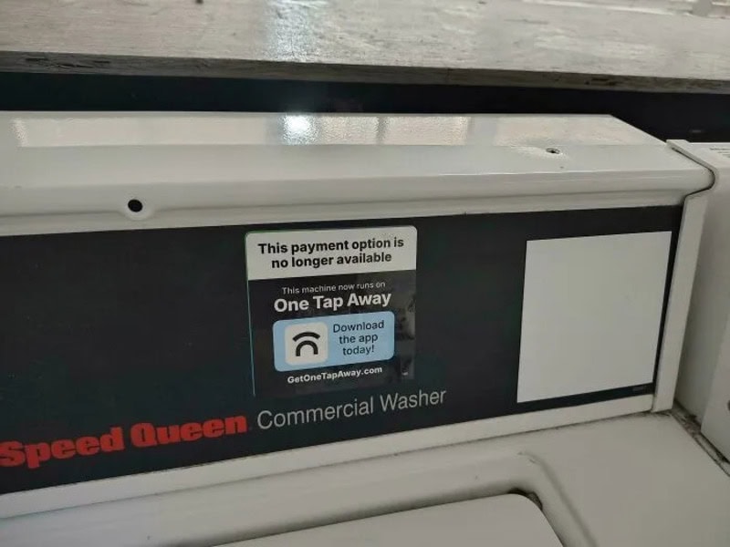 Commercial washer with a sign indicating no longer available payment option.