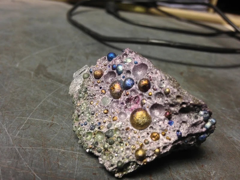 Metallic rock with colorful beads and bubbles on a work surface.