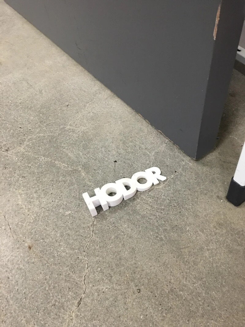 White 3D 'HODOR' sign on concrete floor near gray wall.
