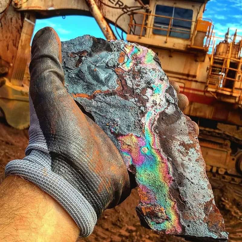 Hand holding a colorful, iridescent mineral sample at a construction site.