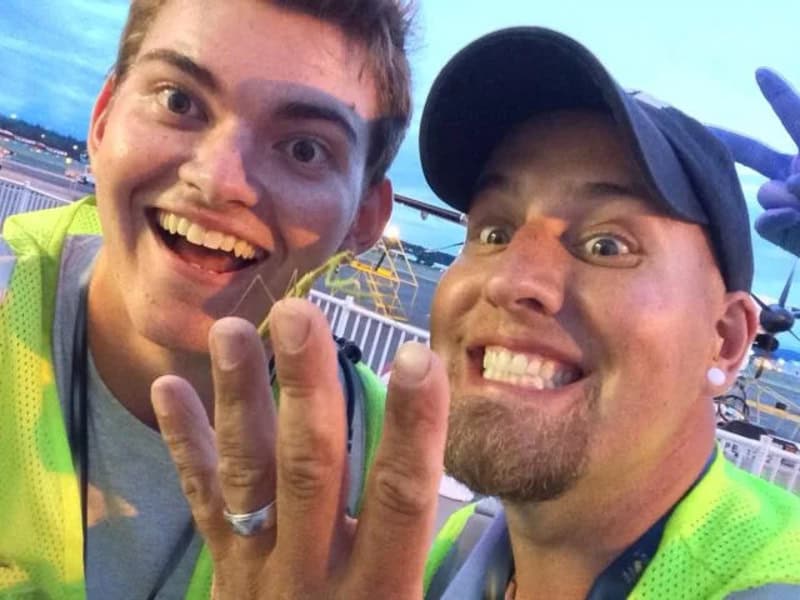 Two men smiling at the camera, one showing a ring on his finger.