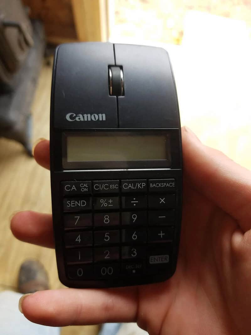 Canon calculator device held in hand with a blurred background.