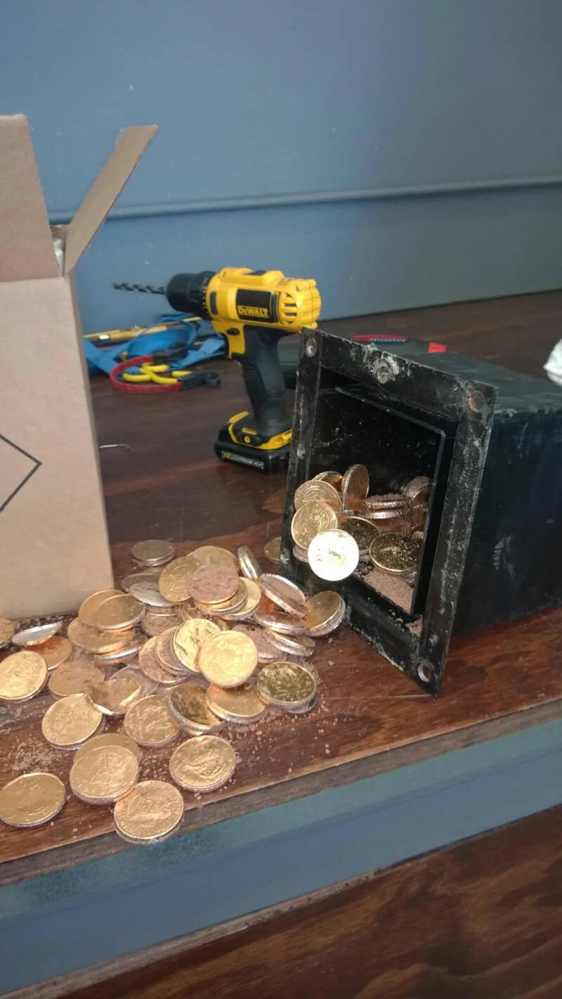 Coins spilled from a black container with a yellow drill in the background.