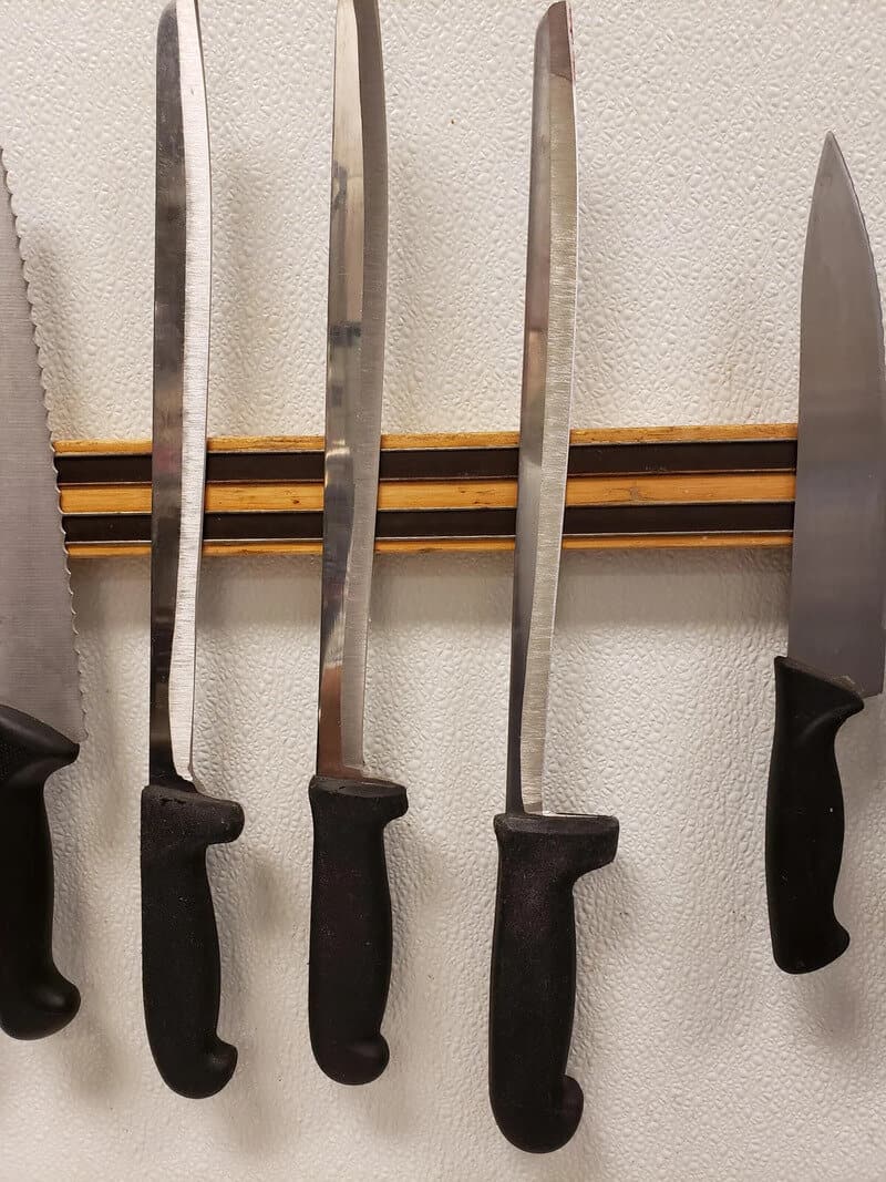 Four knives hanging on a wall with black handles and a wooden rack.