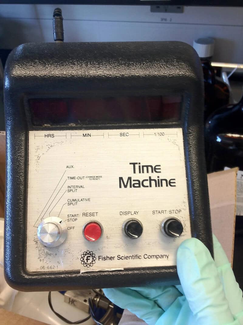 Time Machine device with buttons and display, held by a gloved hand.