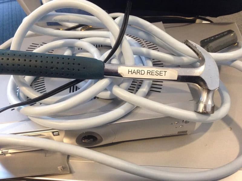 Tangled cables and a hammer labeled 'HARD RESET' on a desk.