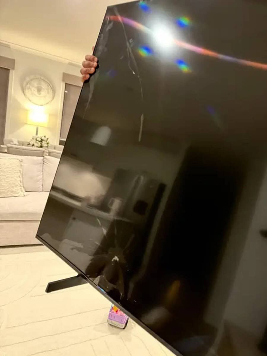 Person holding a large cracked flat-screen TV in a living room.