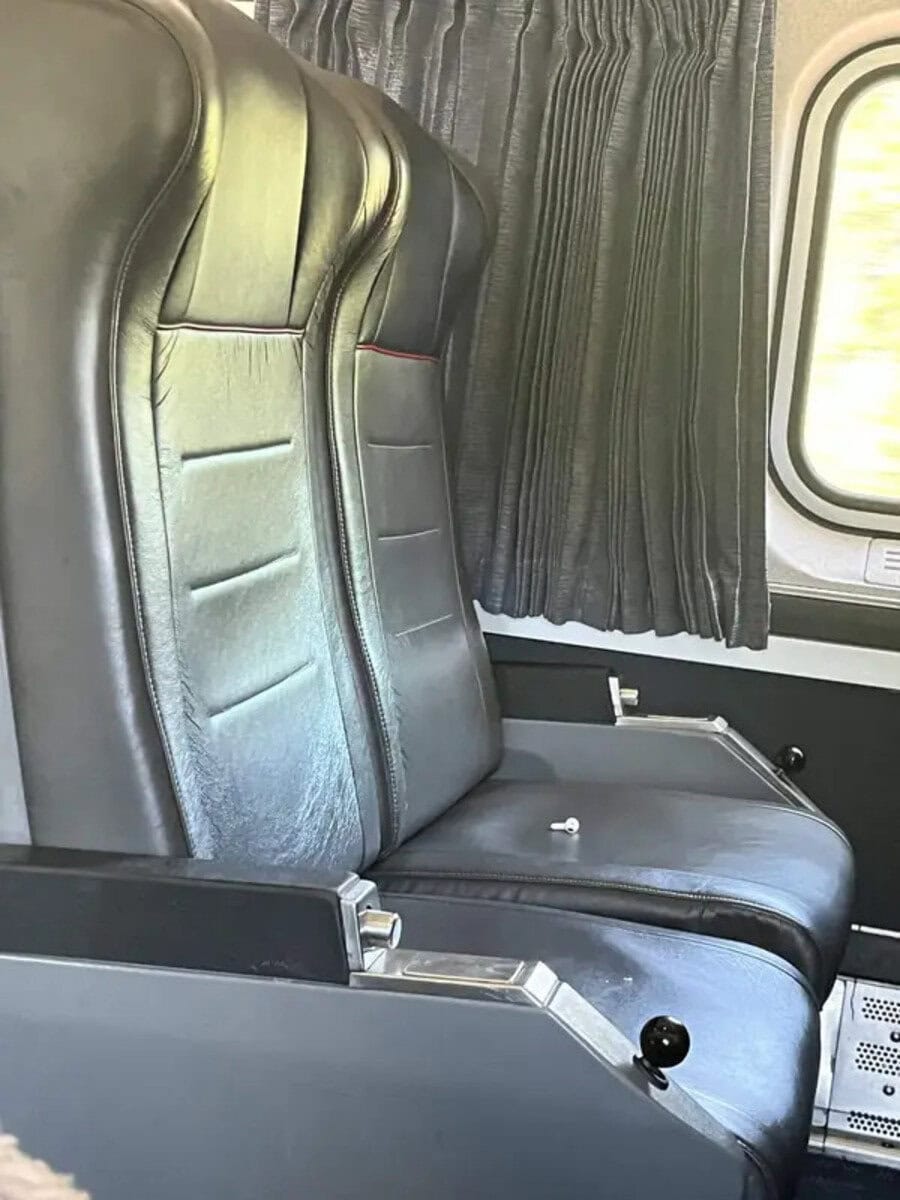 Two black leather airplane seats with a window and curtains in the background.