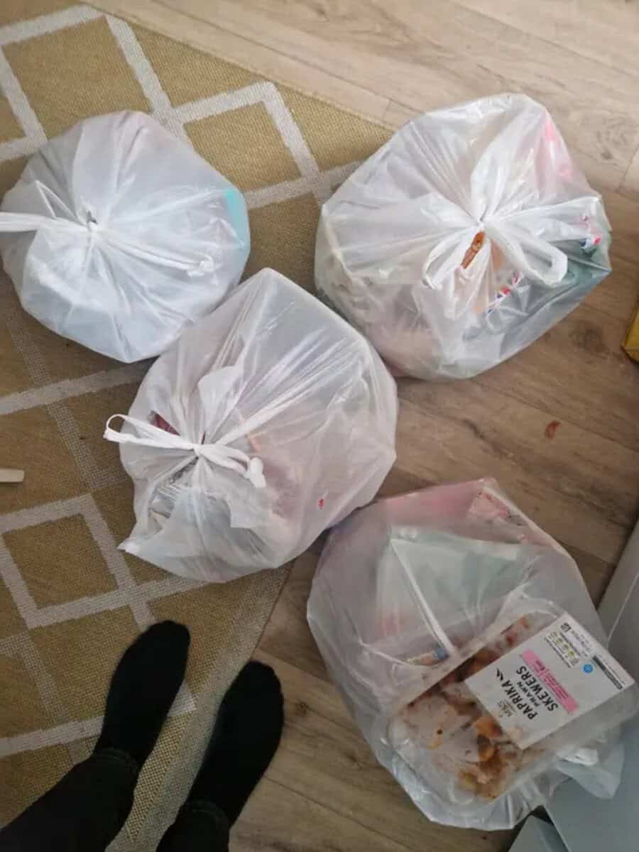 Four white plastic bags on a wooden floor and a rug, with a person's feet visible.
