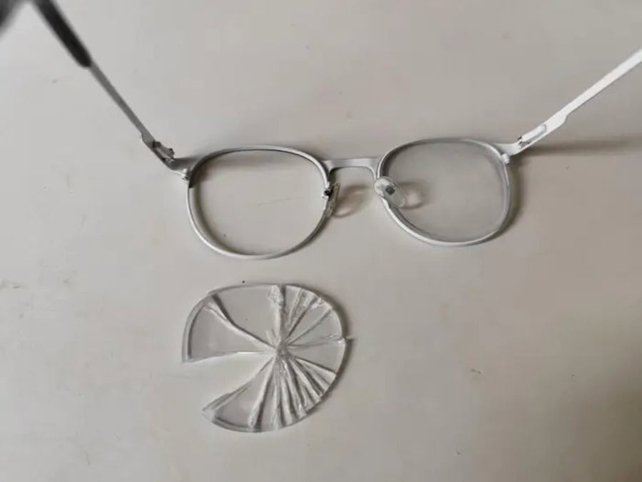 Broken eyeglasses with shattered lens on a white surface.