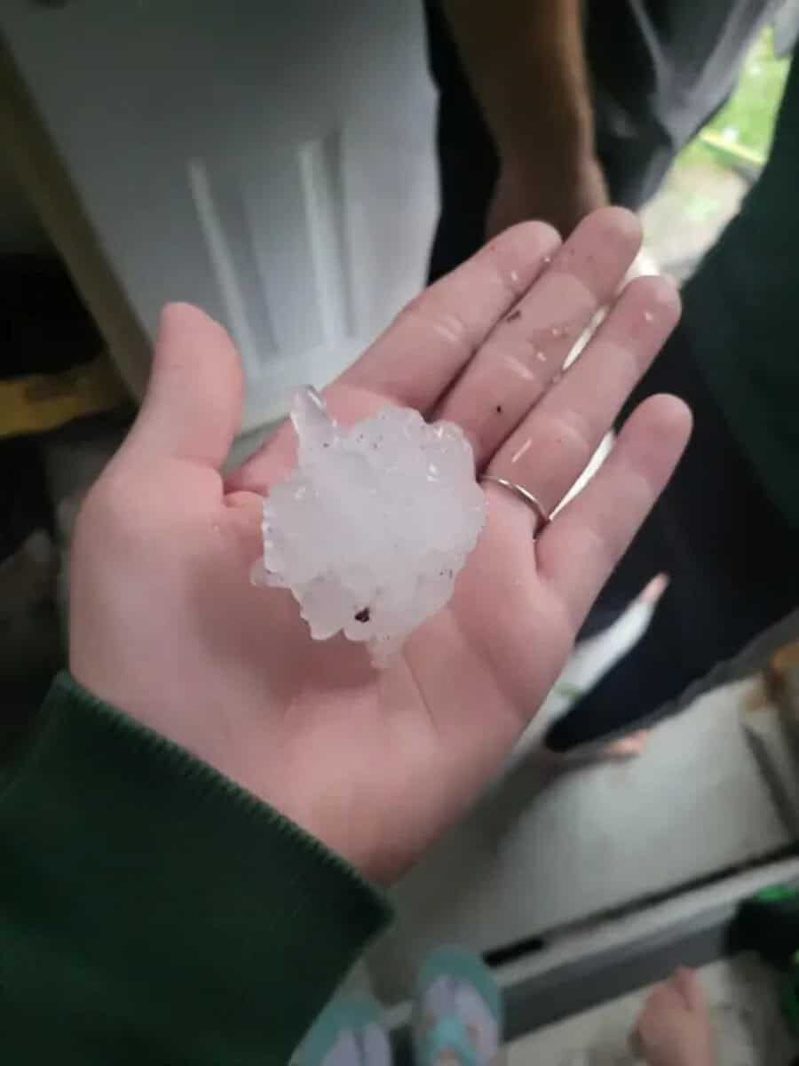 Large hailstone in hand with a door and person in background.