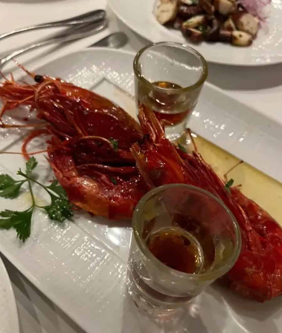 Large cooked prawns with two shot glasses of sauce on a white plate.