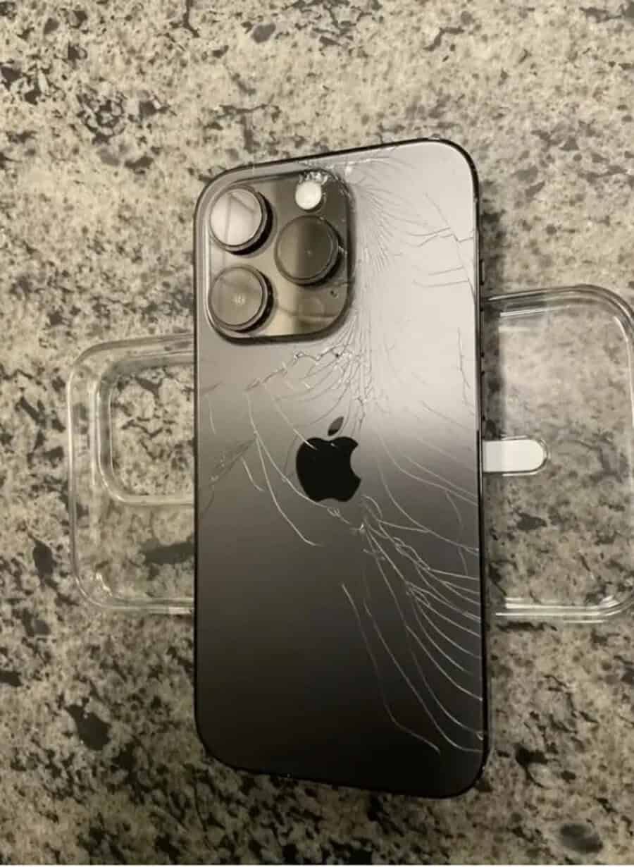 IPhone with cracked back glass on a speckled surface.