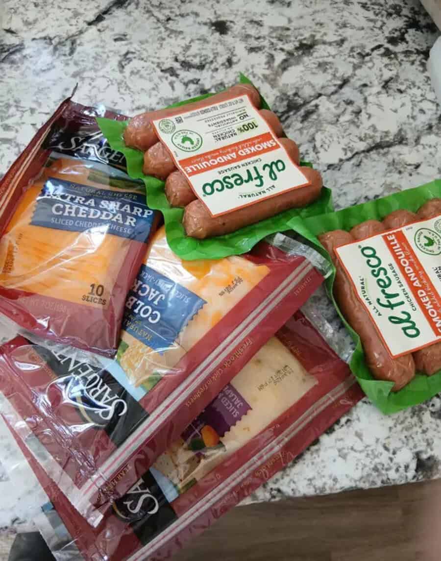 Cheddar cheese, sausage, and sliced cheese on a marble countertop.