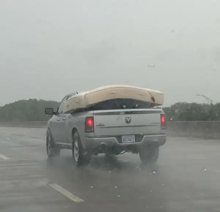 Pickup truck with a kayak on its bed driving in the rain on a highway.