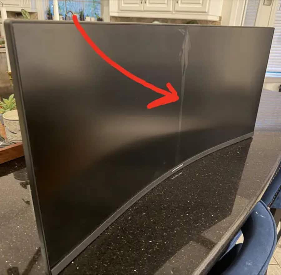 Curved monitor with a vertical crack in the center, marked by a red arrow.