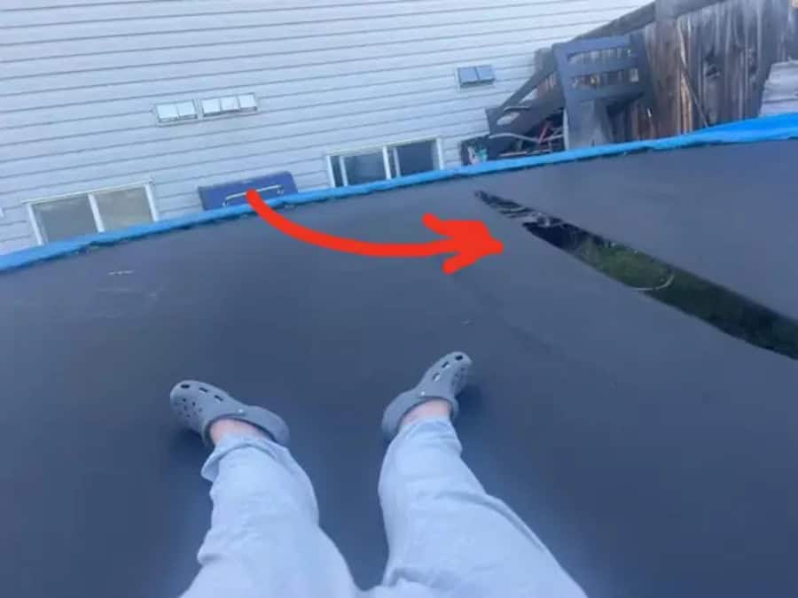 Person sitting on a trampoline with a view of the house and yard.