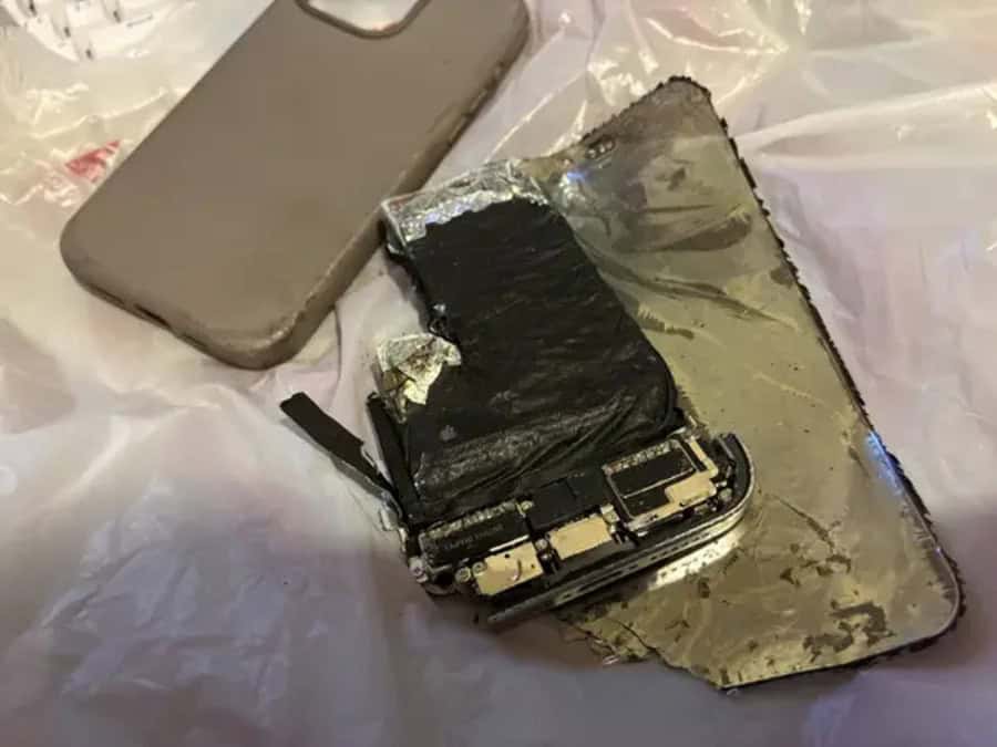 Damaged iPhone with burnt battery and melted components on a plastic surface.