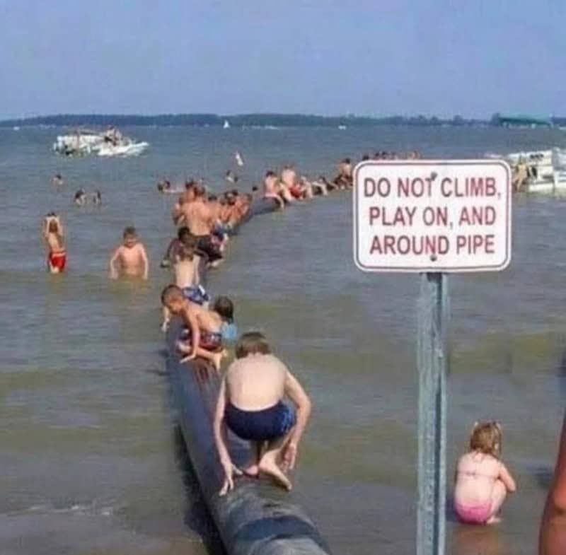 People on a pipe in the water with a sign that says 'Do not climb, play on, and around pipe'.
