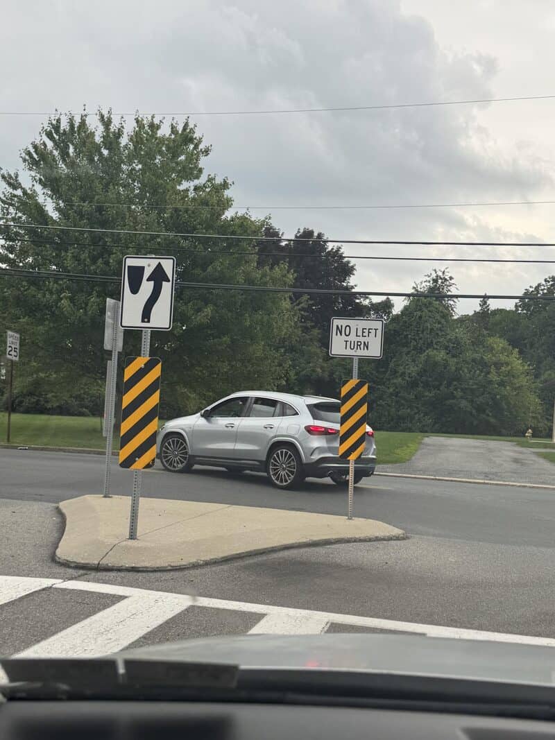 Car on a roundabout with no left turn sign and a right turn arrow sign.