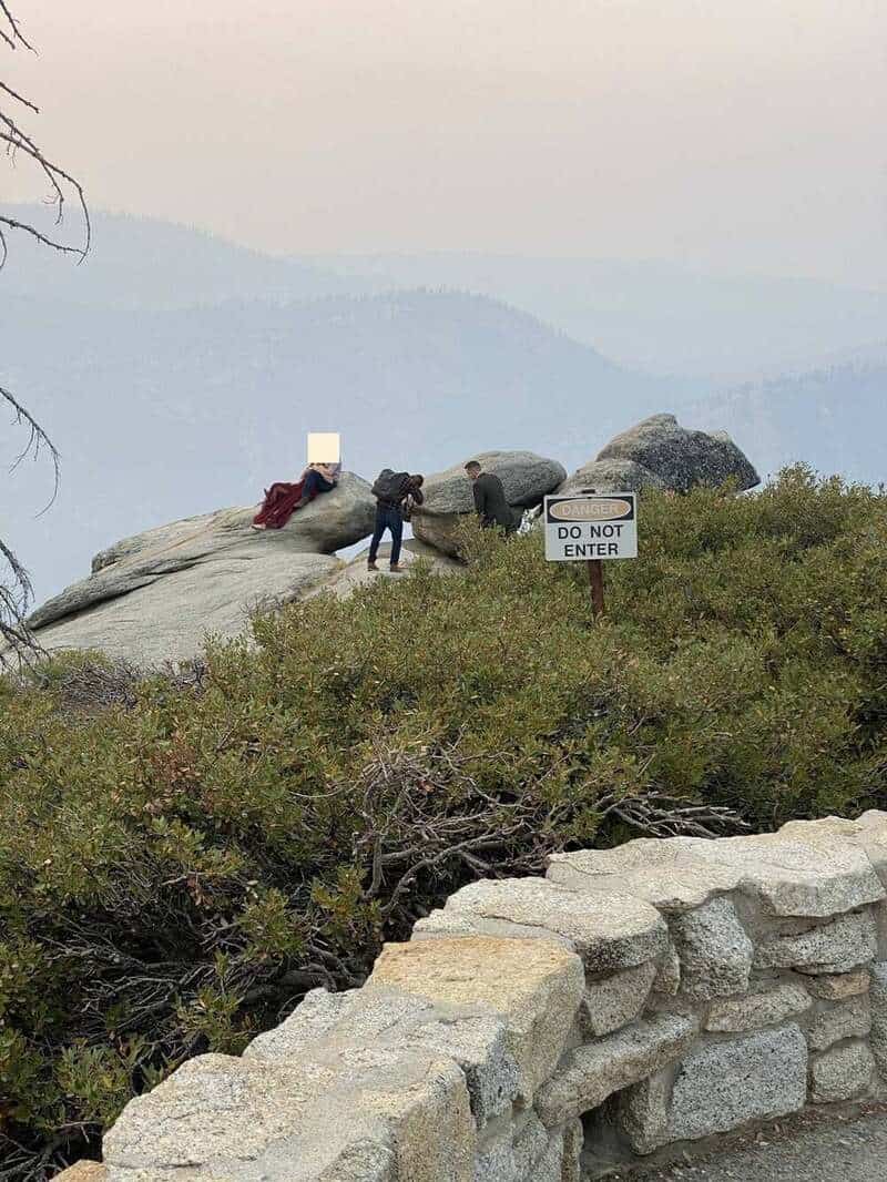 People on rocks near a 'Do Not Enter' sign with mountains in the background.