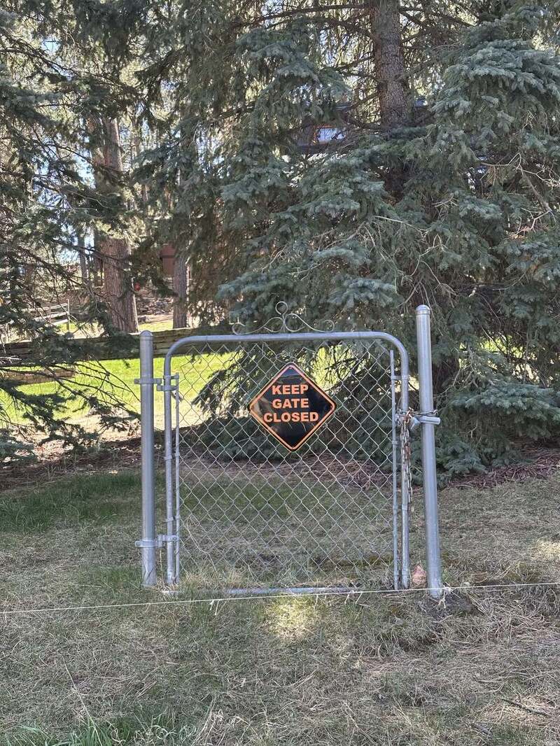 Keep gate closed sign on a chain-link gate in front of trees.