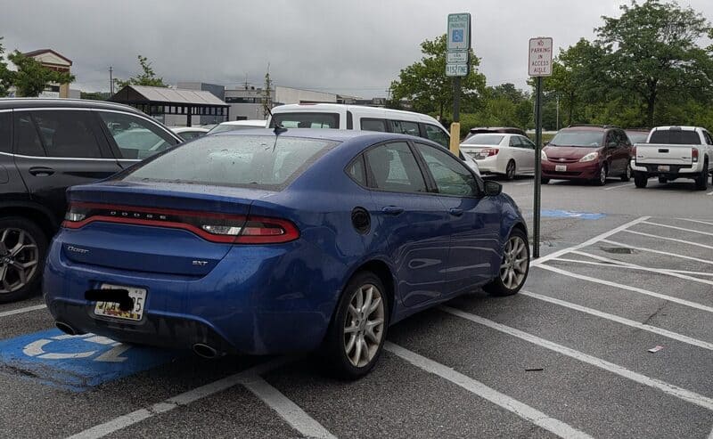 Blue sedan parked in a handicapped space on a rainy day.