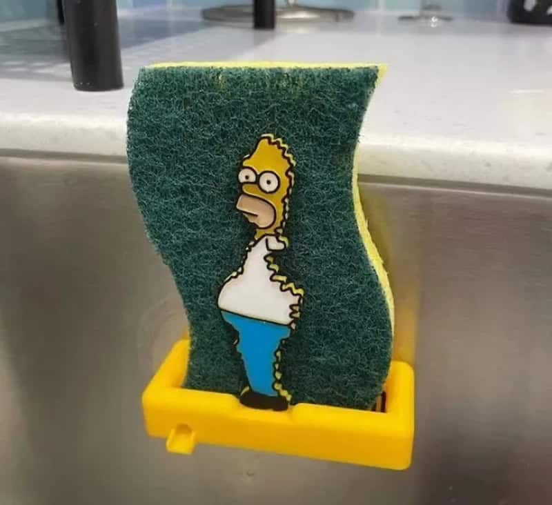 Cleaning sponge with Homer Simpson image, yellow holder, in sink.